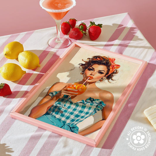 a framed illustration of a woman drinking a cocktail, surrounded by a pink and white striped tablecloth, lemons, strawberries, and a cocktail glass.