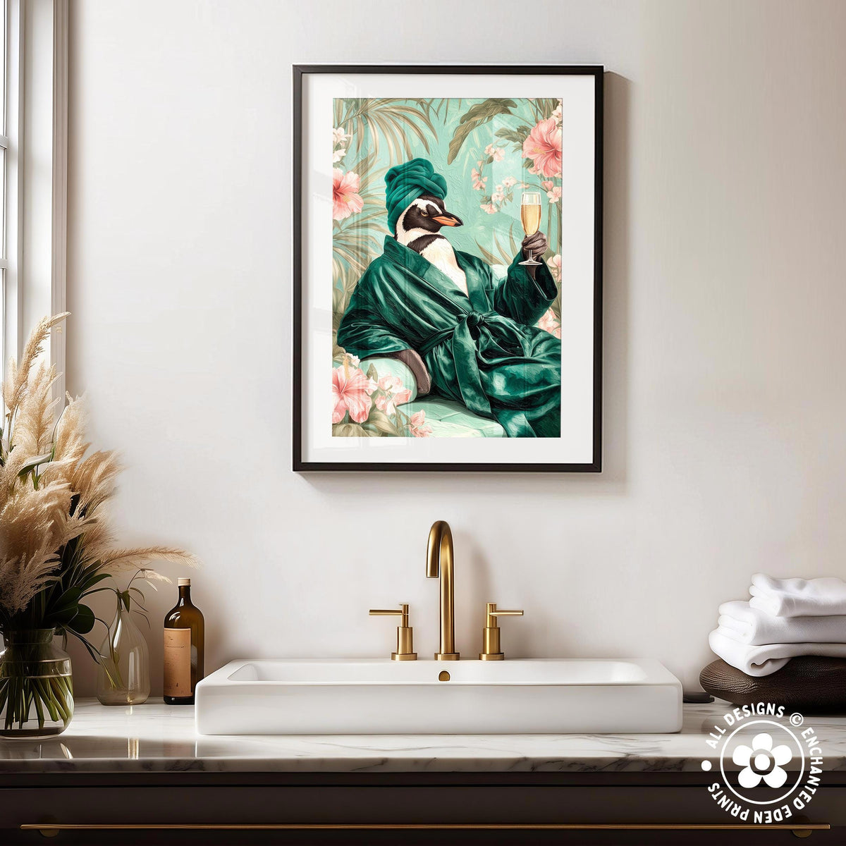 a framed print of a penguin wearing a green robe and hat, holding a glass of wine, sitting on a bench and holding a book. The penguin is surrounded by a tropical garden scene with pink flowers and green foliage. The sink is located below the framed print, and there are decorative items such as a vase and a bottle on the countertop.