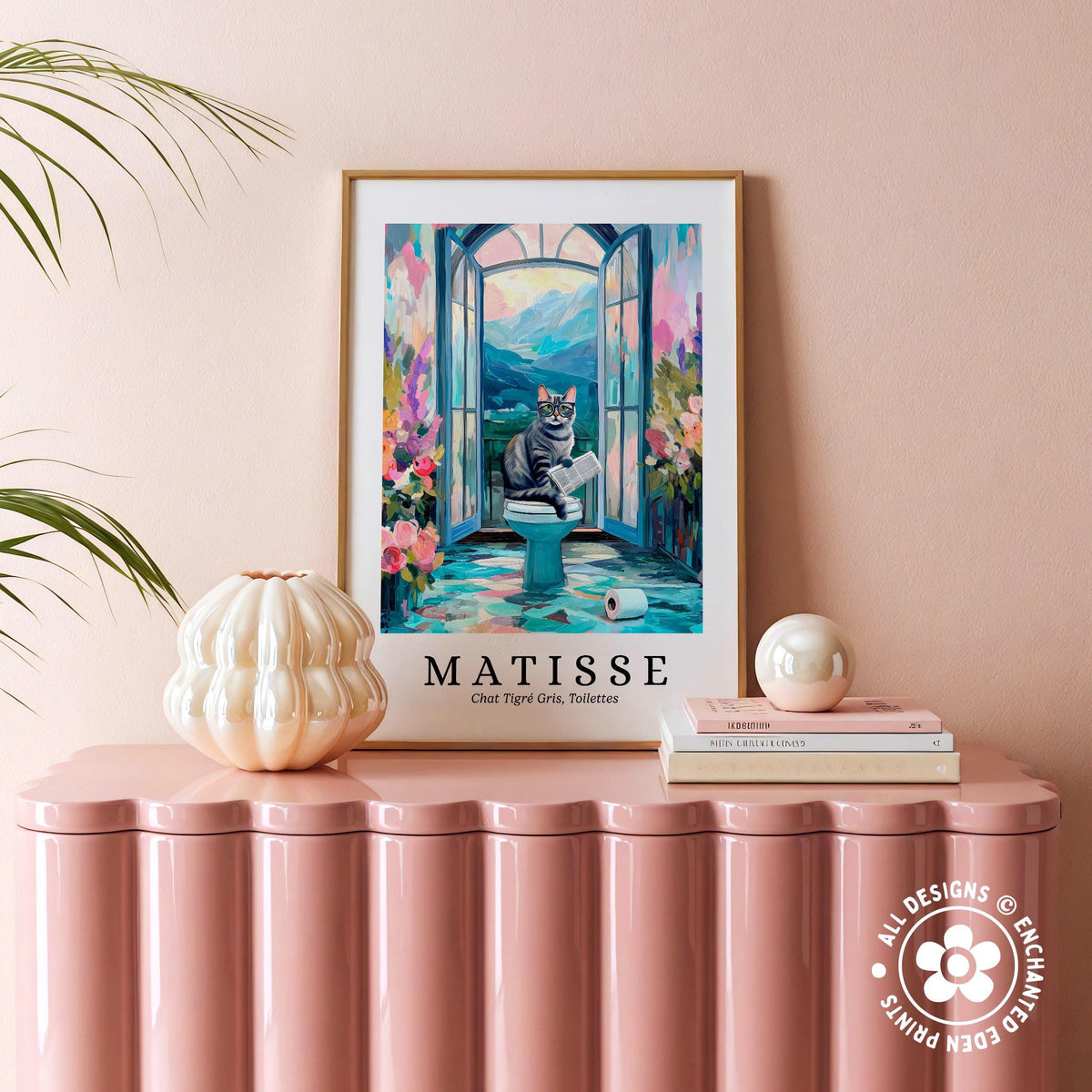 a framed painting of a cat sitting on a toilet, surrounded by a colorful and whimsical scene, placed on a pink table.