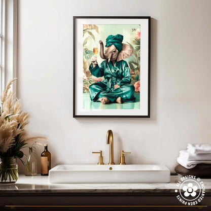 a framed print of an elephant wearing a green robe and holding a glass of wine, sitting on a green surface. The elephant is surrounded by a tropical landscape, including palm trees and flowers. The sink in the bathroom has a gold faucet, and there are some decorative items on the counter, such as a vase and a bottle.