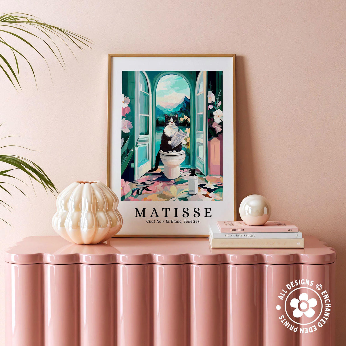 a pink table with a framed poster of a cat sitting on a toilet in an open doorway, surrounded by flowers and plants.