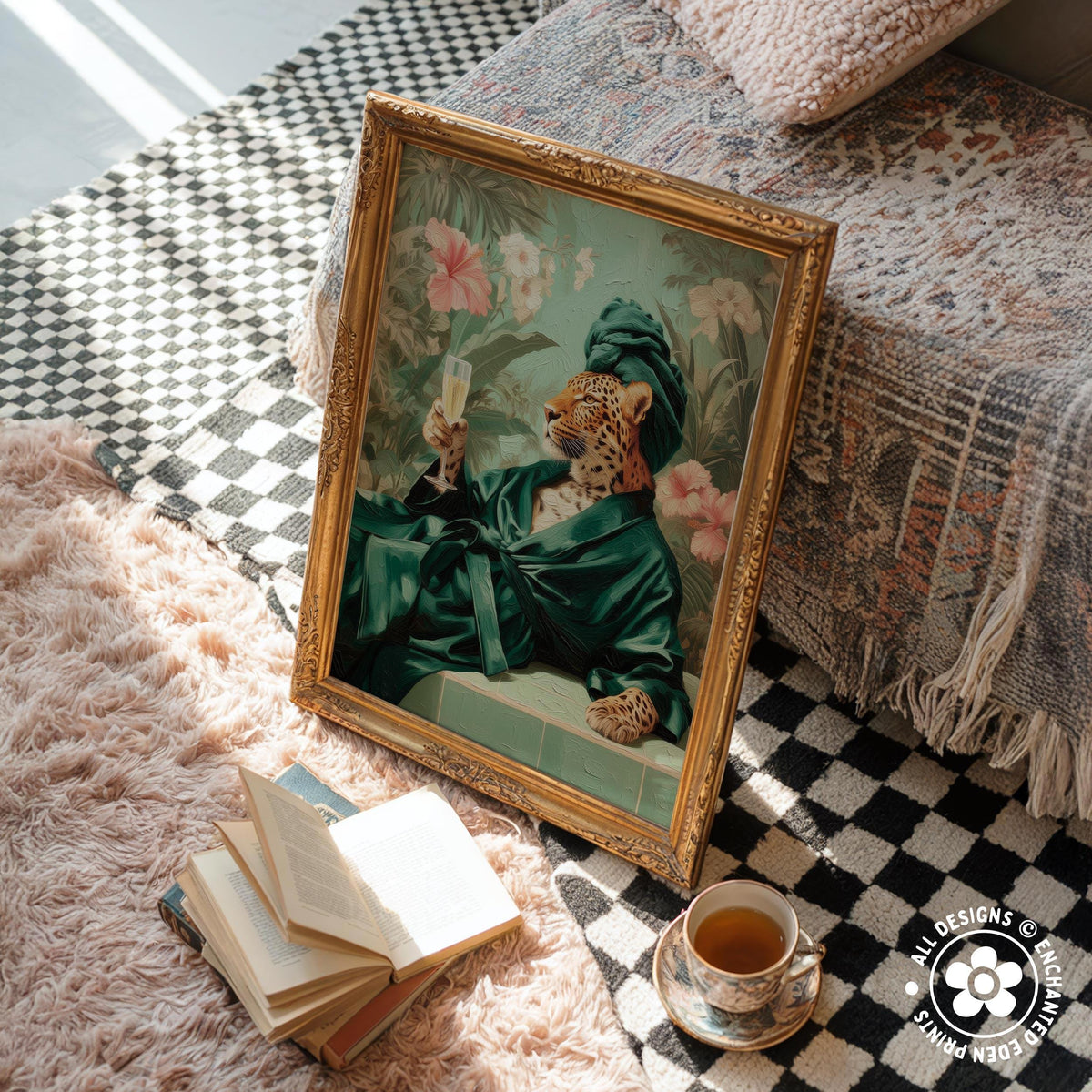 a framed painting of a leopard wearing a green robe and holding a glass of wine, placed on a checkered rug next to a stack of books and a cup of tea.