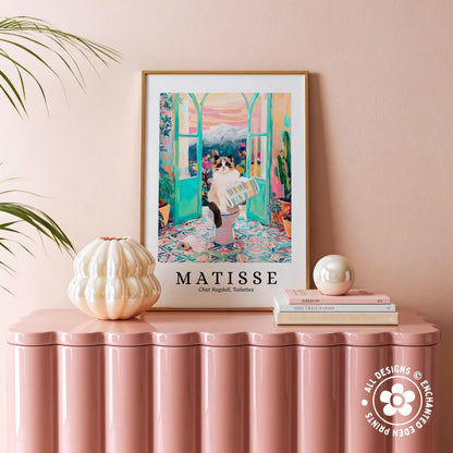 a pink table with a framed poster of a cat in a colorful, artistic room, surrounded by various decorative items such as a white vase, a stack of books, and a small white ball.
