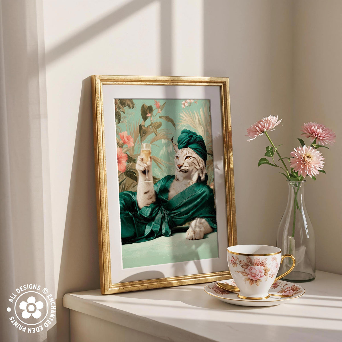 A framed picture of a cat wearing a green robe and hat, sitting on a table next to a vase of pink flowers and a cup of tea.