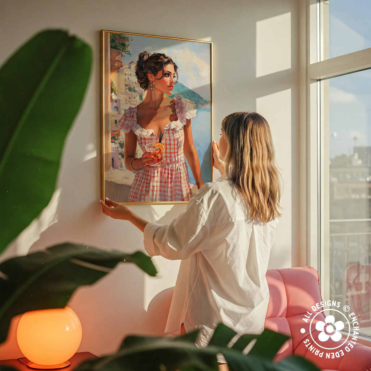 A woman hangs a framed painting of a woman in a red and white dress on a wall in a room with a pink chair and a plant.