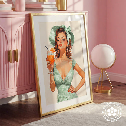 A framed illustration of a woman in a green dress holding a drink, with a pink cabinet and a lamp in the background.