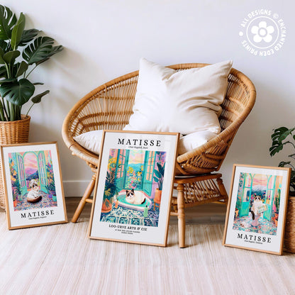 three framed prints of the famous painting "Matisse" by Edgar Degas, including a large print of a cat sitting on a chair and two smaller prints of the same cat in different poses. The prints are displayed on a wooden floor in front of a wicker chair, with potted plants in the background.