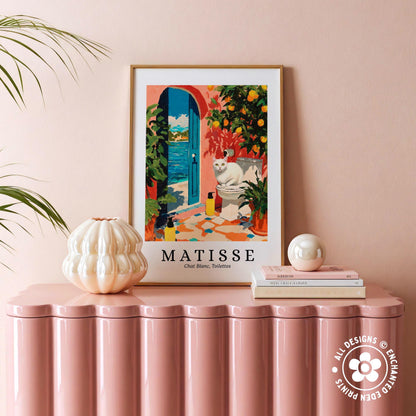 a framed painting of a cat sitting on a windowsill, with a pink table in the foreground.