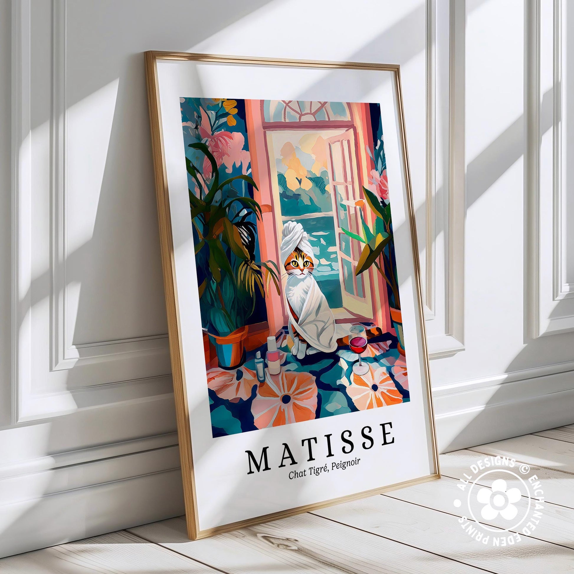 A framed poster depicting a cat wrapped in a towel, sitting on a windowsill with a potted plant and flowers in the background, against a white wall.