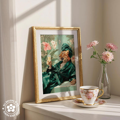 a framed painting of a jaguar wearing a green robe and holding a glass of champagne, placed on a white shelf next to a vase of pink flowers and a cup of tea.