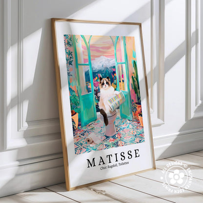 A framed poster depicting a cat sitting on a toilet in a colorful, whimsical setting, with a mountain landscape in the background.