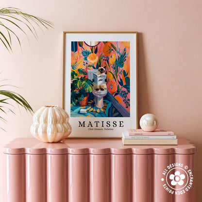 a pink table with a framed poster of the painting "Matisse" hanging on it, along with a white vase and a stack of books.