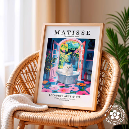 A framed poster of a cat sitting in a bathtub, surrounded by colorful flowers, is displayed on a wicker chair.