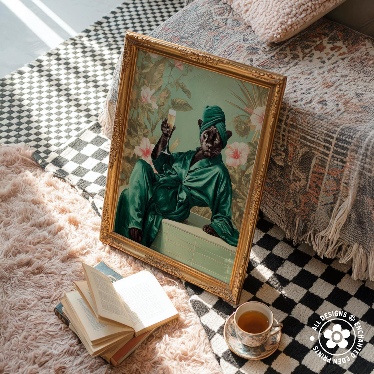 a framed painting of a cat dressed in a green robe, sitting on a bed and holding a glass of wine. The painting is placed on a pink shag rug, with a stack of books and a cup of tea nearby.