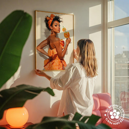 A woman hangs a framed painting of a woman in an orange dress on a wall, with a pink chair and a green plant in the foreground.