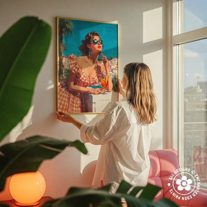A woman hangs a framed painting of a woman in a red and white dress on a wall, with a pink chair and a plant in the foreground.