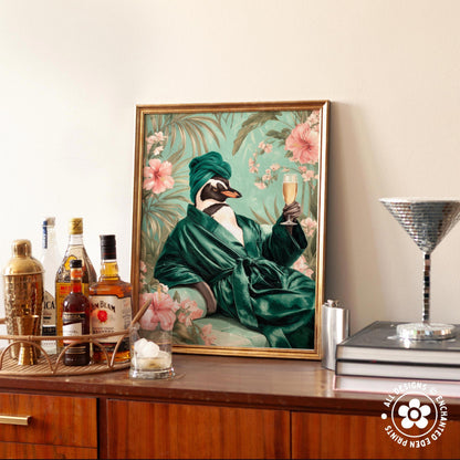 a framed painting of a penguin wearing a green robe and holding a glass of champagne, surrounded by a floral background.