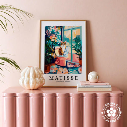 a framed poster of a cat sitting on a pink stool, with a window and plants in the background, placed on a pink table.
