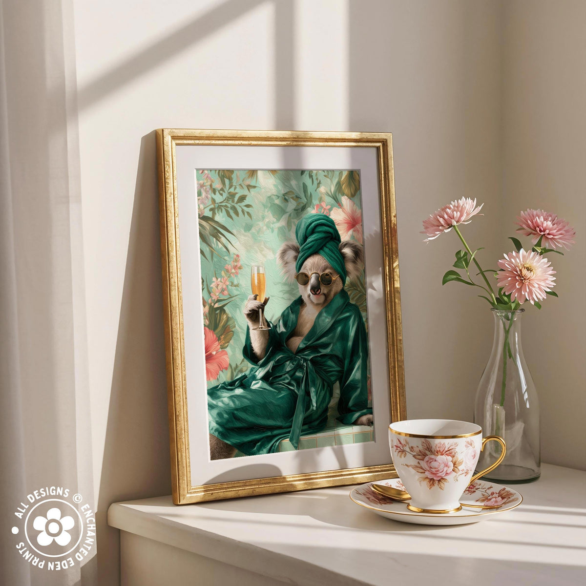 A framed painting of a koala wearing a green robe and holding a champagne glass is displayed on a white shelf next to a vase of pink flowers and a teacup.