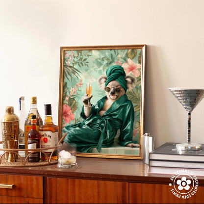 A framed painting of a koala wearing a green robe and holding a glass of wine, surrounded by various bottles of alcohol and a cocktail shaker on a wooden surface.