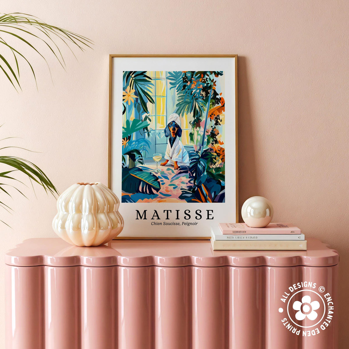 a pink table with a framed poster of a colorful tropical scene hanging above it, along with a stack of books and a small white vase on the table.